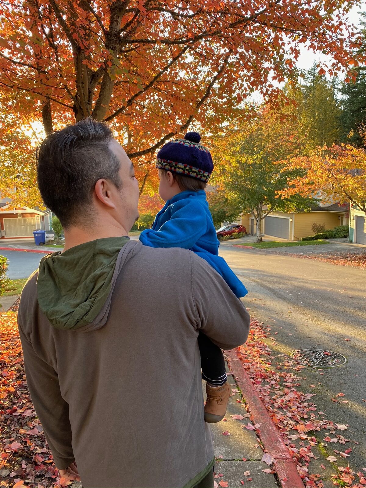 Christopher carrying his daughter on his shoulders under fall foliage