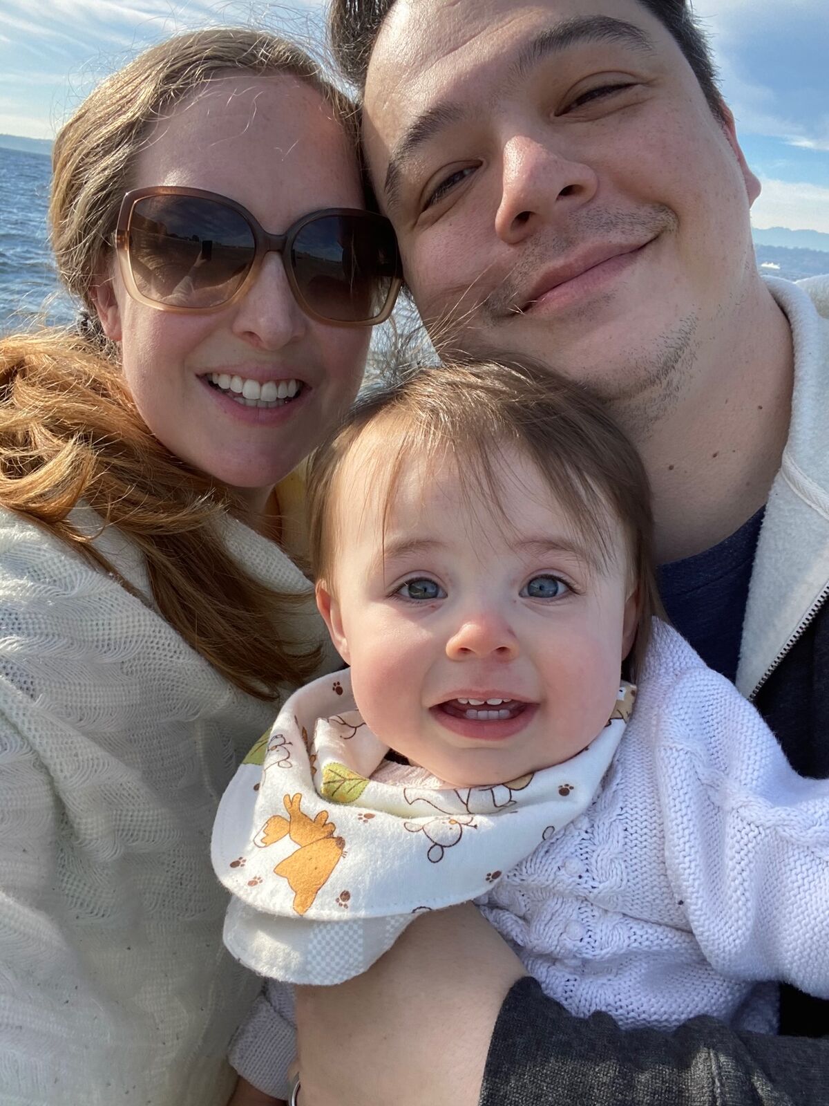 Christopher with his spouse and daughter on a sunny day by the water