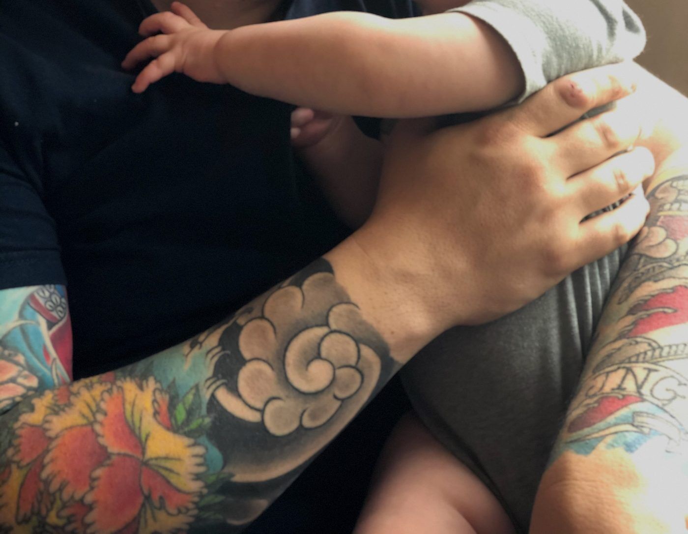 Christopher holding his daughter's hand, tattoos visible on his forearm